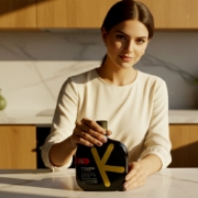Beautiful woman presenting a bottle of premium Greek olive oil in an upscale kitchen, part of an elegant gourmet gift set
