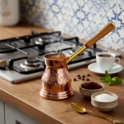 Artisanal copper briki steaming on a modern gas stovetop, ready to serve traditional Greek coffee
