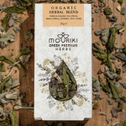 Top-down view of the Mouriki Organic Herbal Blend box surrounded by loose dried herbs including Malotira leaves and orange peel on a rustic wooden surface.