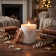 Lit Lumos candle by Aurean Golden placed on a rustic wooden table with vintage books, creating a cozy ritual of comfort.