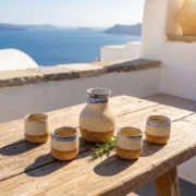 Luxury handmade ceramic carafe set on a wooden table overlooking the blue Aegean sea and caldera in Santorini.